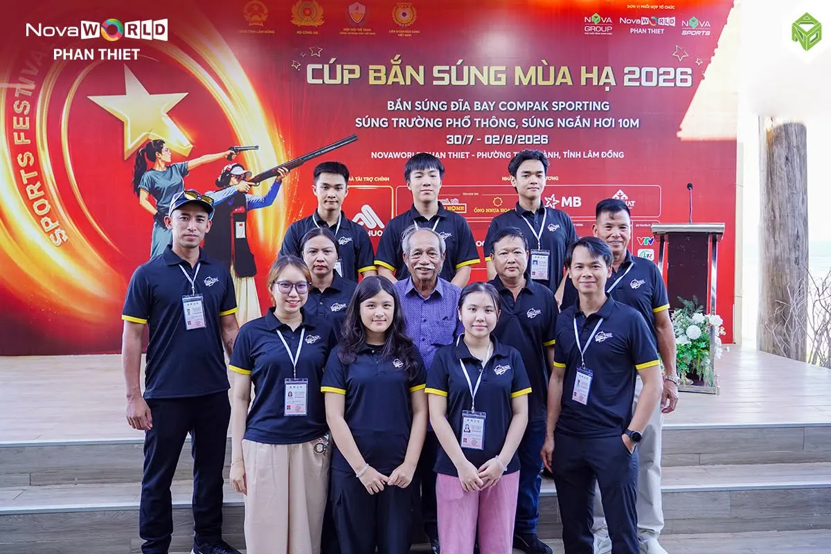 Nhóm khoảng mười bốn người mặc áo đen đứng chụp ảnh chung trước phông giải trong lễ khai mạc