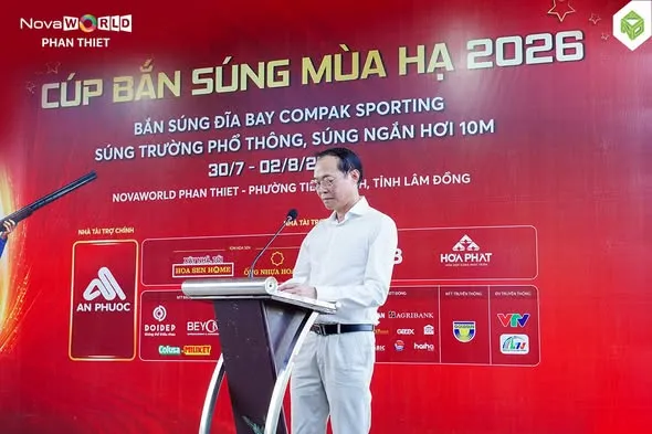 Người phát biểu đứng tại bục trong lễ khai mạc, phía sau là phông đỏ lớn có dãy biểu trưng nhà tài trợ