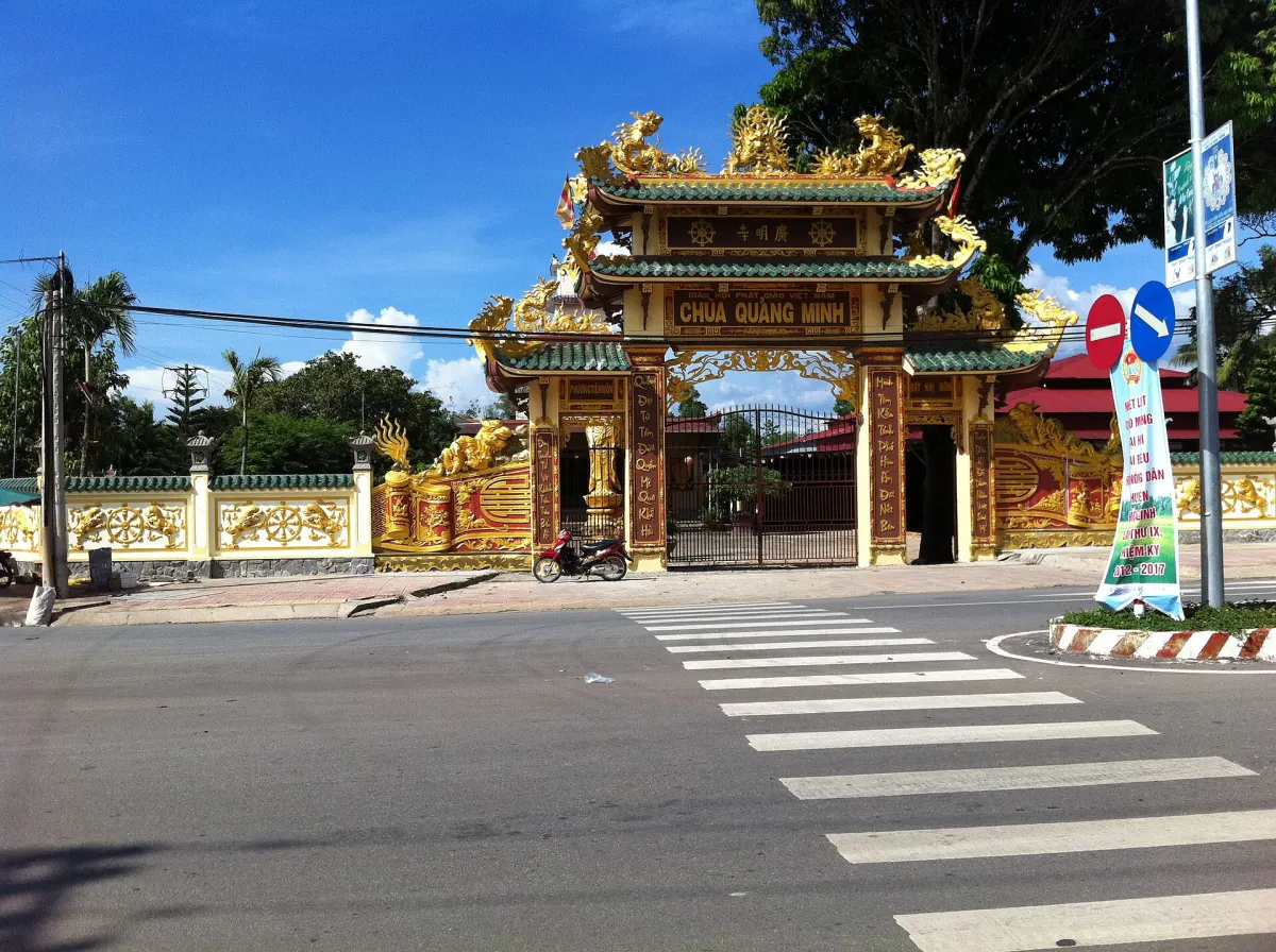 Cổng tam quan chùa sơn vàng với mái cong nhiều tầng, đứng ngay bên đường nhựa có vạch qua đường